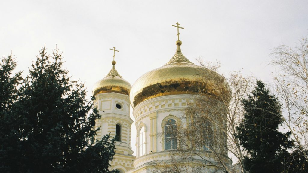 Золотые купола белокаменной церкви, виднеются через кроны деревьев