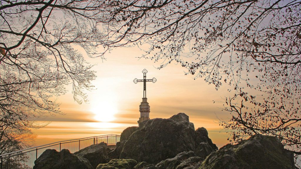 Крест стоящий на вершине скалы, под ветвями осенних деревьев, на фоне утреннего неба