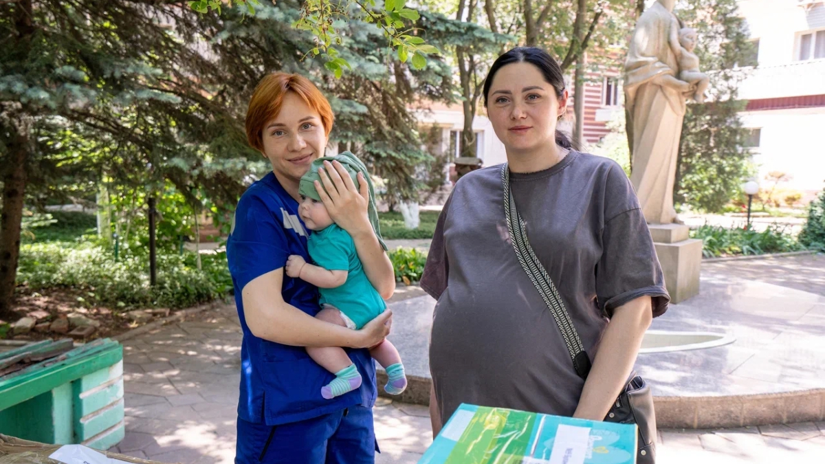 Девушка в положении рядом с медсестрой, у которой на руках младенец