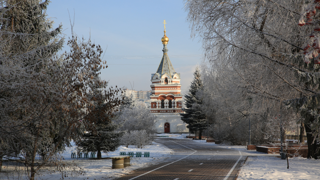Красно-белая церковь виднеется через заснеженные деревья