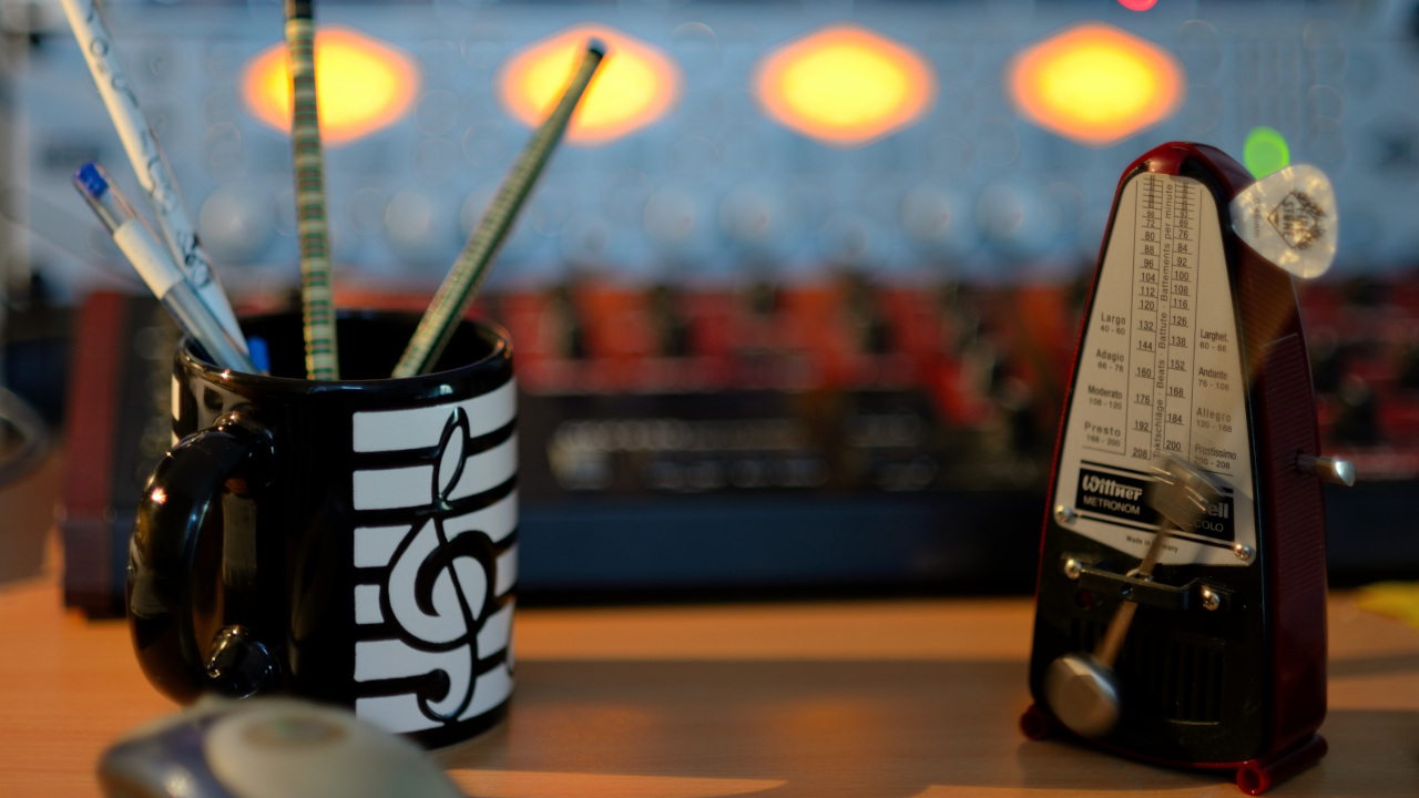 Метроном стоит на столе рядом с кружкой: с карандашами: перед звуковым пультом