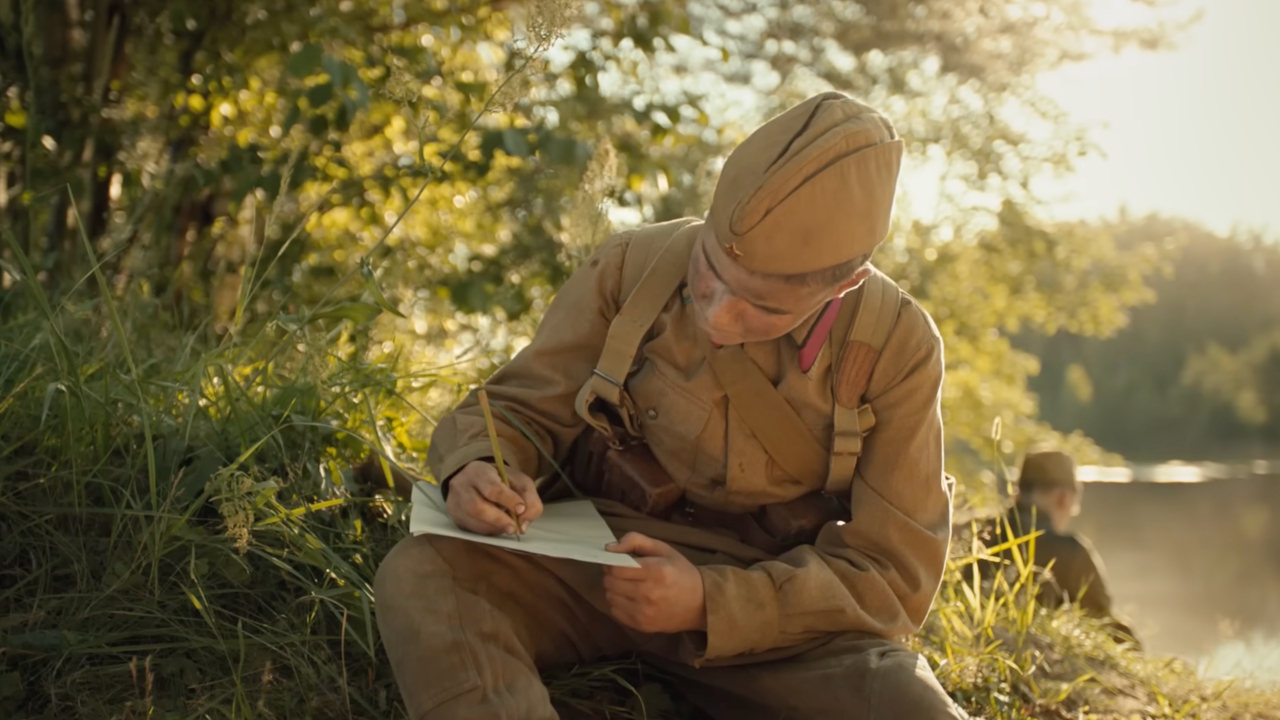 Солдат пишет письмо, сидя на берегу реки